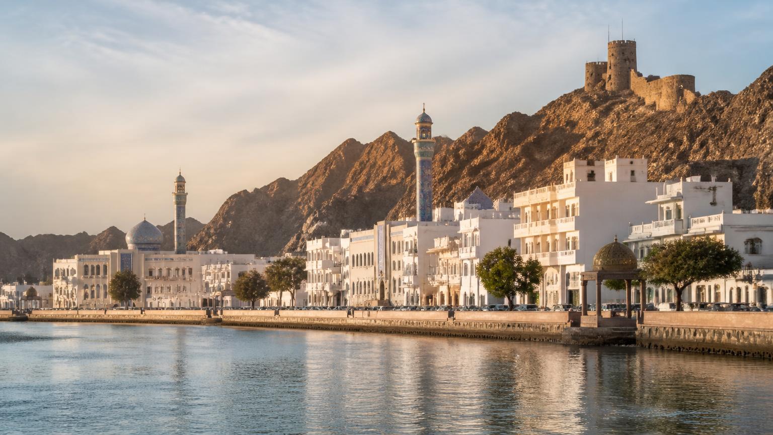 De corniche van Muttrah in Muscat met witte gebouwen, minaret en een fort op de heuvel